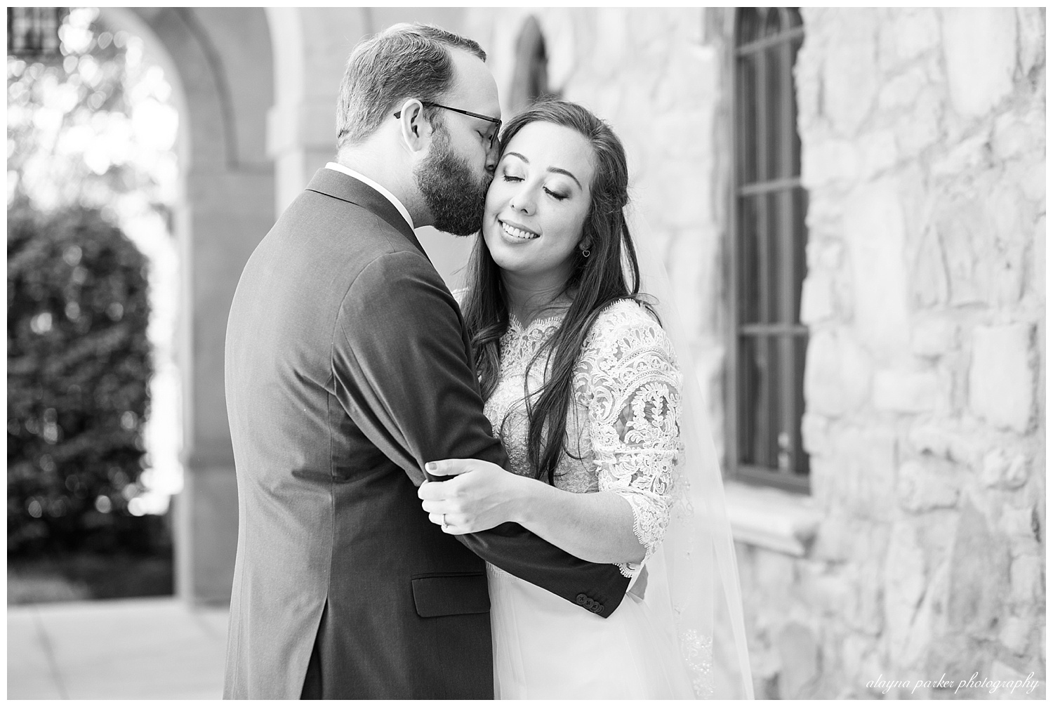 black and white image of groom kissing bride while bride smiles and closes her eyes