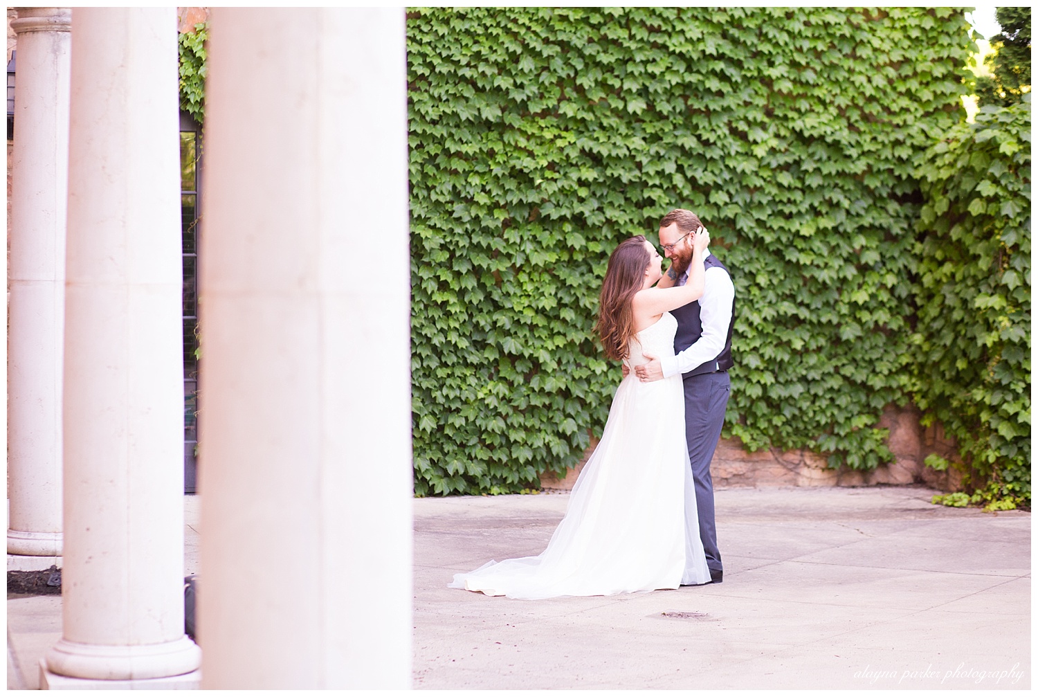 bride holding back of groom's head in front of ivy wall and columns at club at corazon