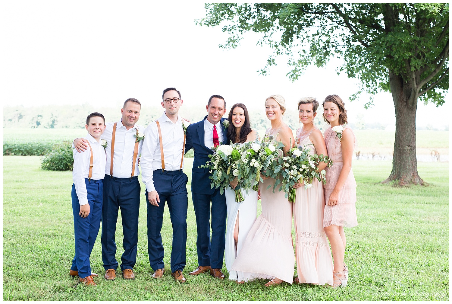 bridesmaids in pink dresses and groomsmen in navy pants, white shirts, and leather suspenders
