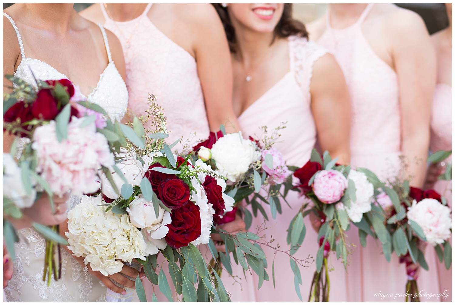 close up of girls in pink dresses holding bouquets of white, red, and pink flowers and eucalyptus