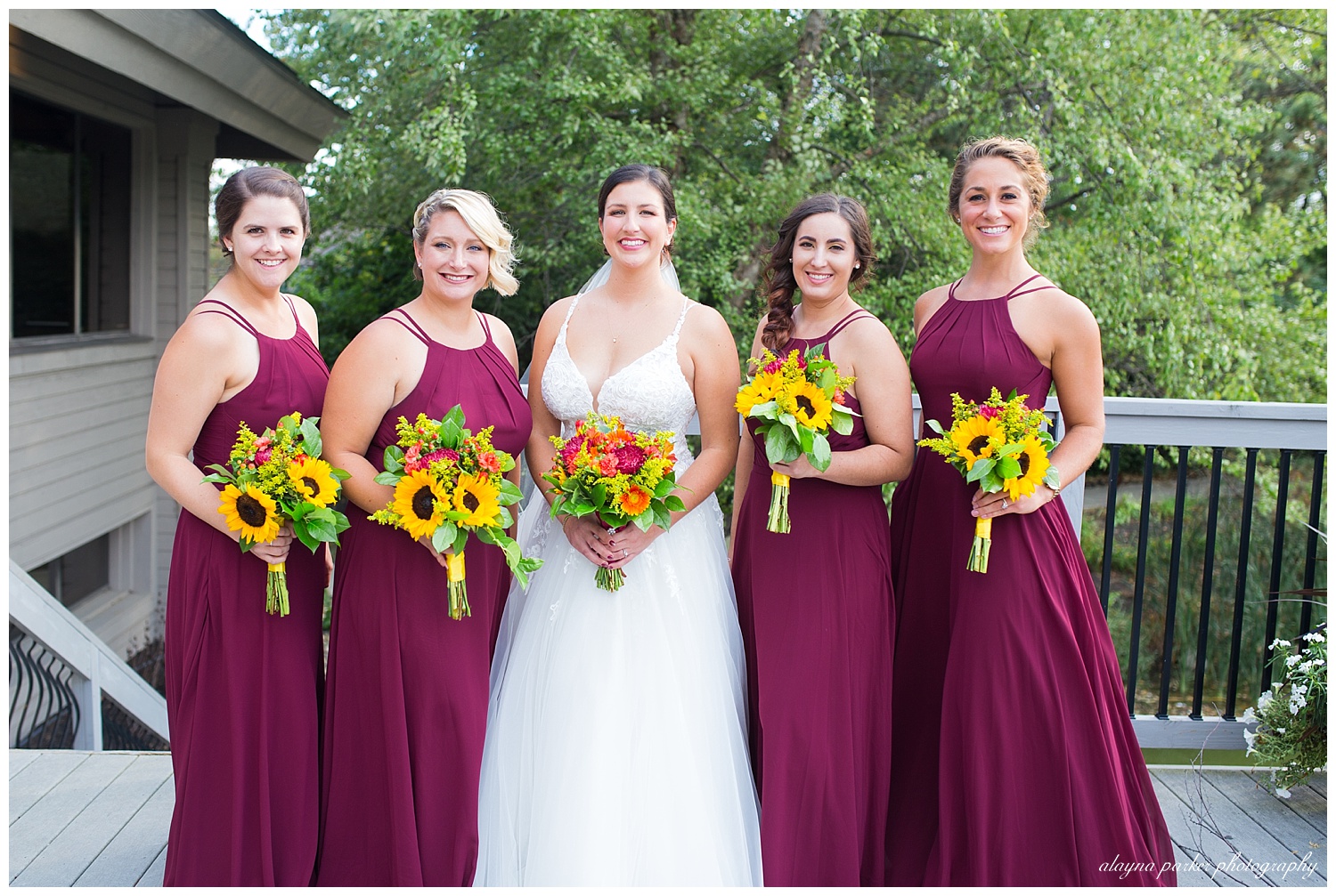 bride and bridesmaids smiling at camera outside at water's edge