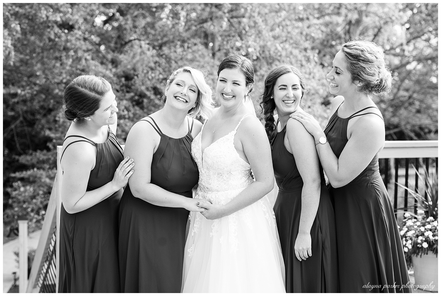 black and white image of bride and bridesmaids laughing outside at water's edge