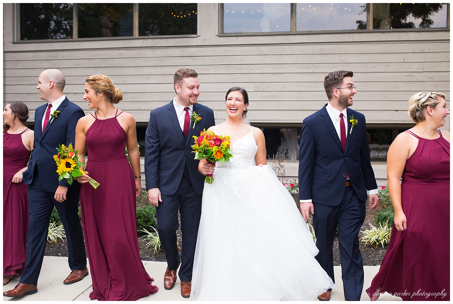 bride and groom laughing while walking with bridal party outside at water's edge