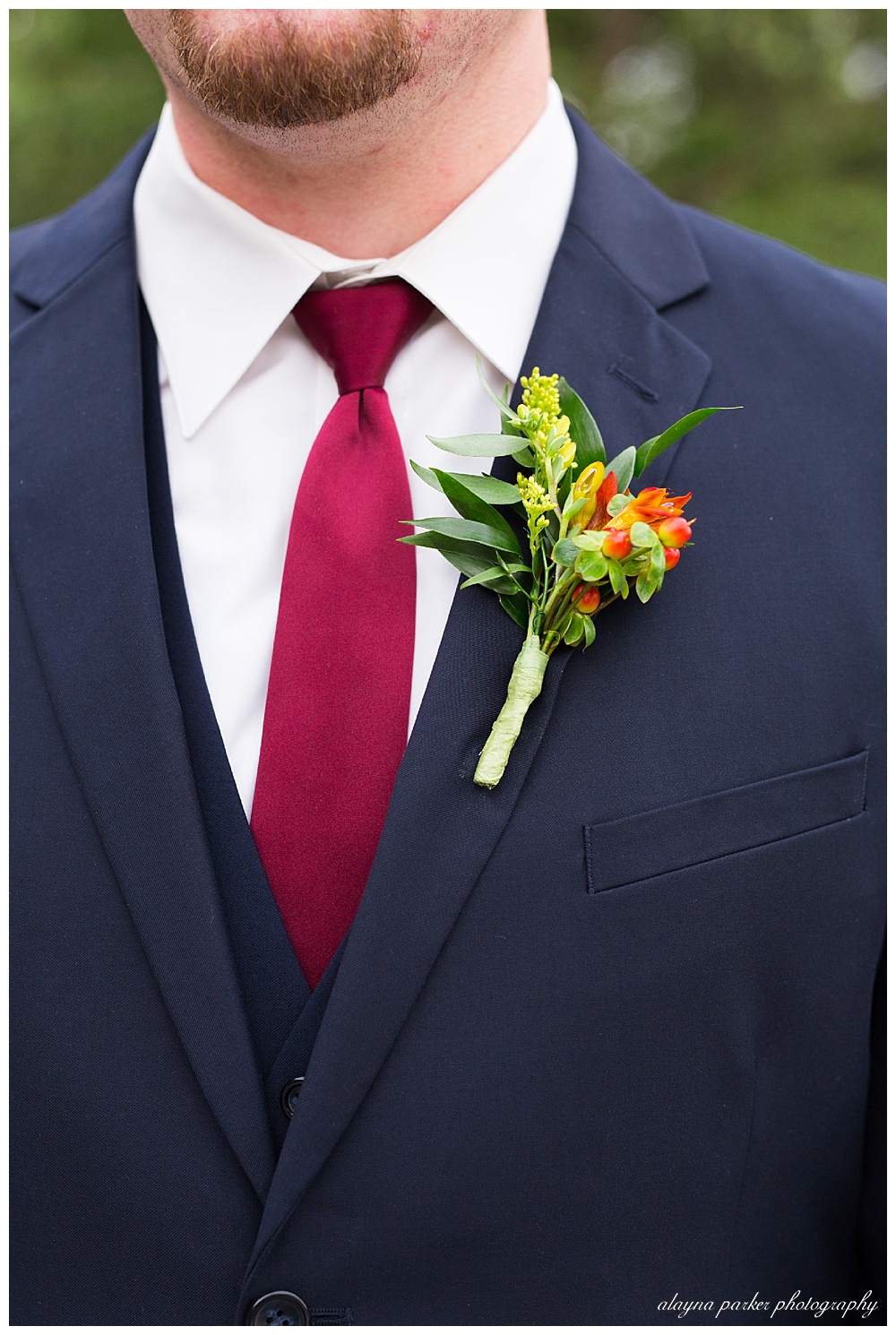 close up of groom's boutonniere with green leaves, orange flowers, and yellow flowers