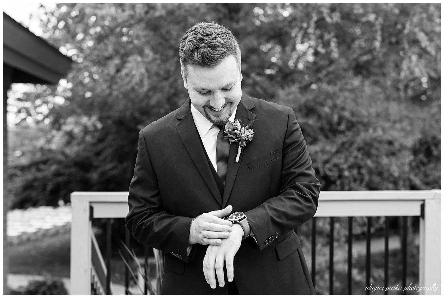 black and white image of groom smiling and looking at watch