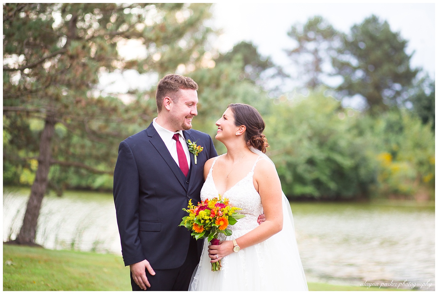 bride and groom looking at each other with pond behind them at water's edge