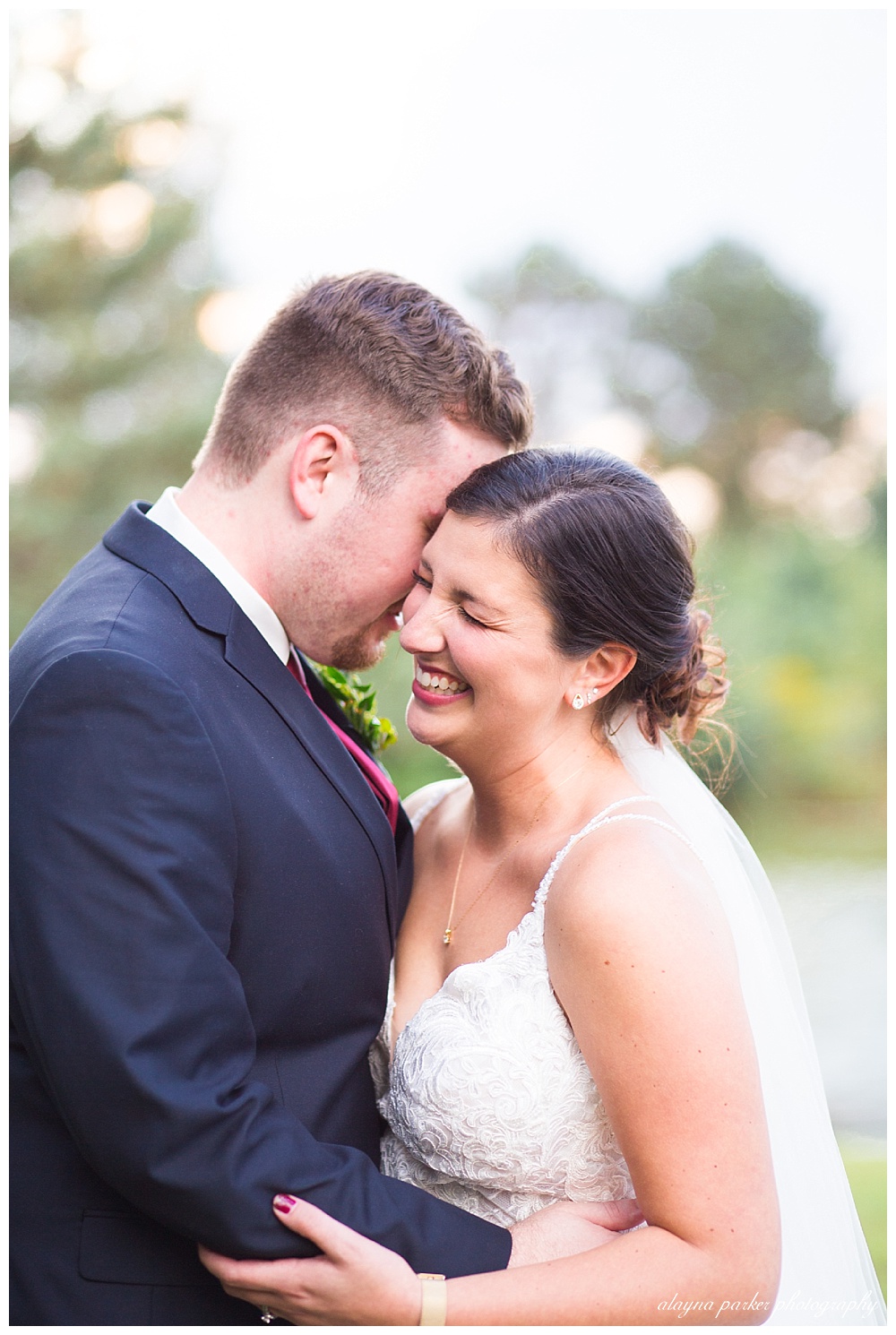 bride laughing while groom whispers in her ear at water's edge