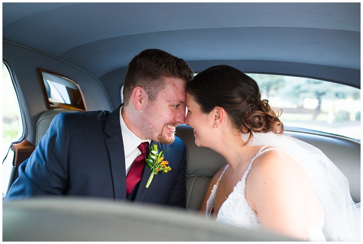 bride and groom touching foreheads in the backseat of a white 1960's classic car at water's edge