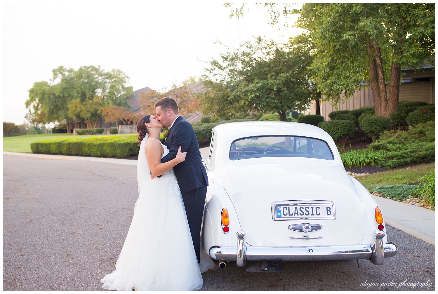 bride and groom kissing beside a white 1960's classic car at water's edge