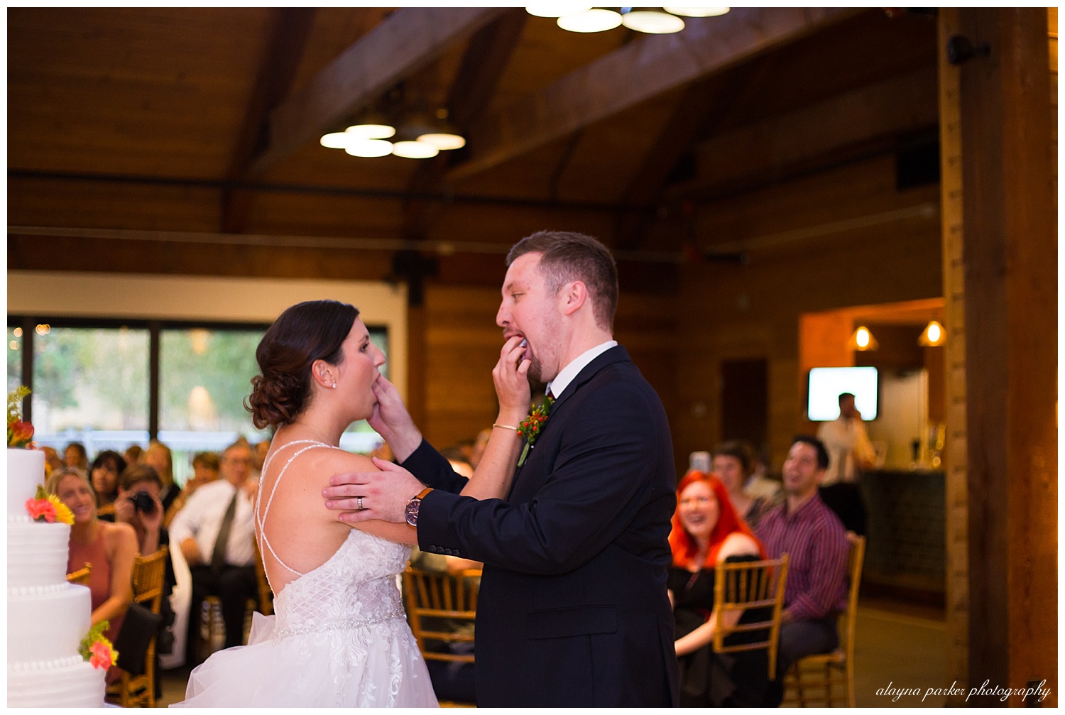 bride and groom feeding each other cake at water's edge