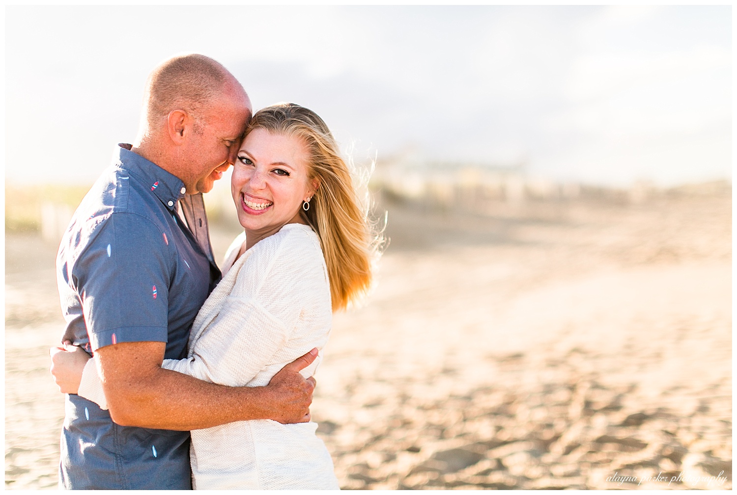 woman looking at camera while man snuggles into her on beach in outer banks
