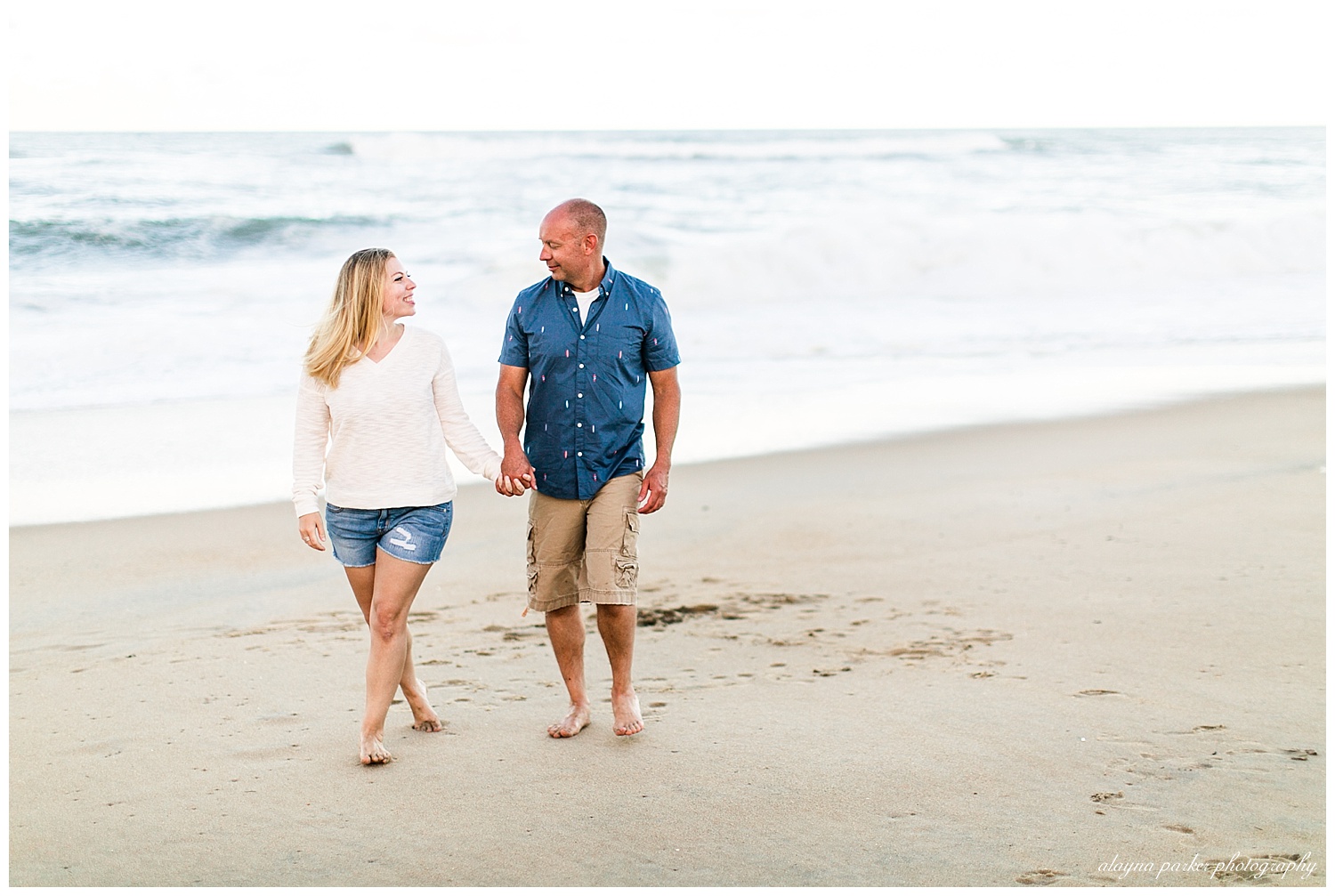 couple holding hands walking along beach in outer banks