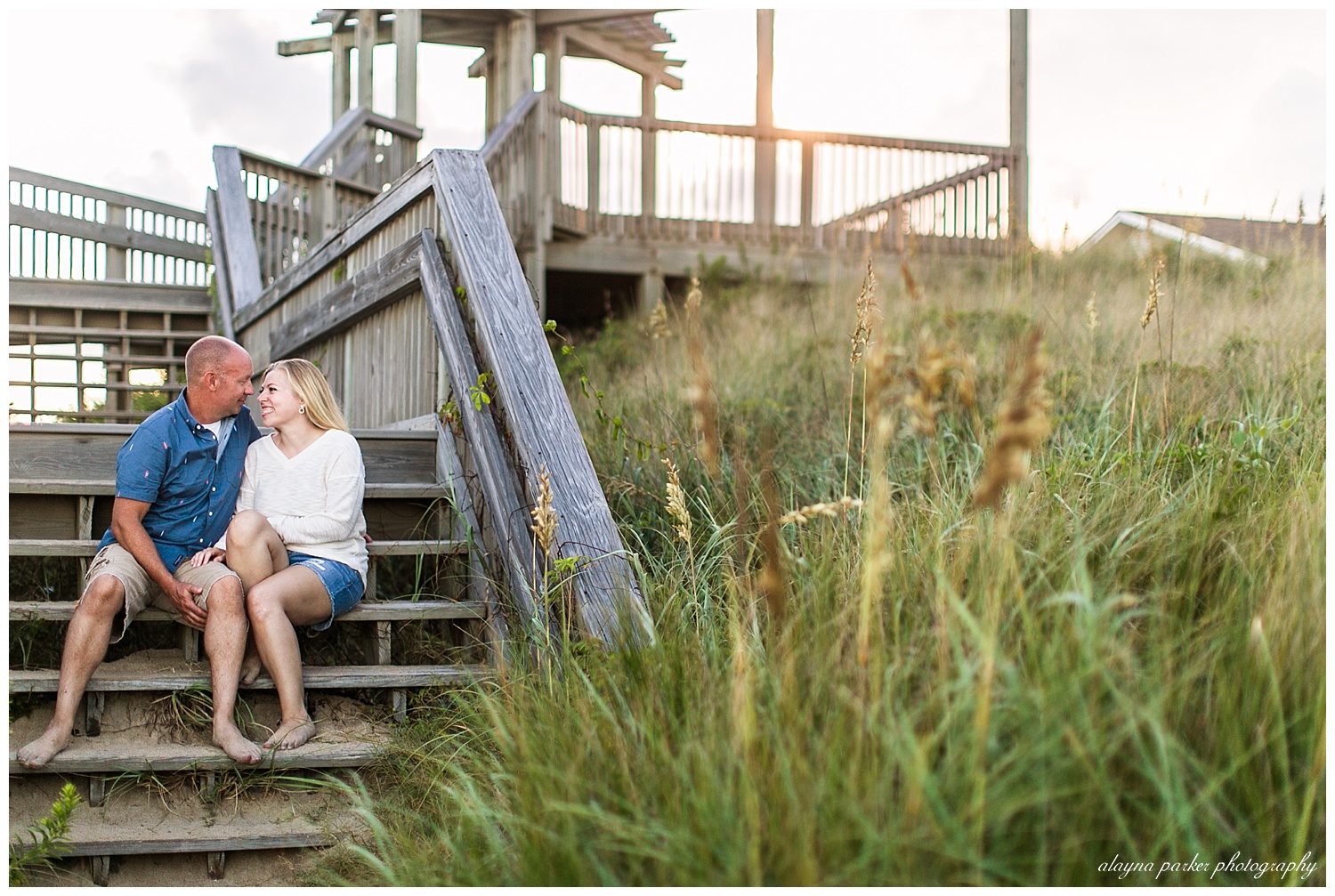 couple looking at each other and smiling while sitting on walkway on beach in outer banks