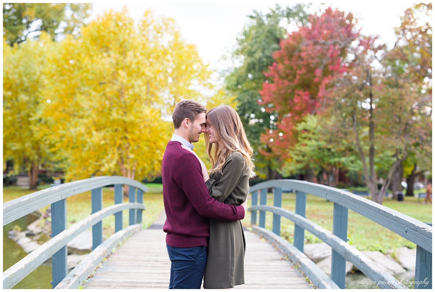 couple touching foreheads with colorful trees in background on bridge at schiller park in german village