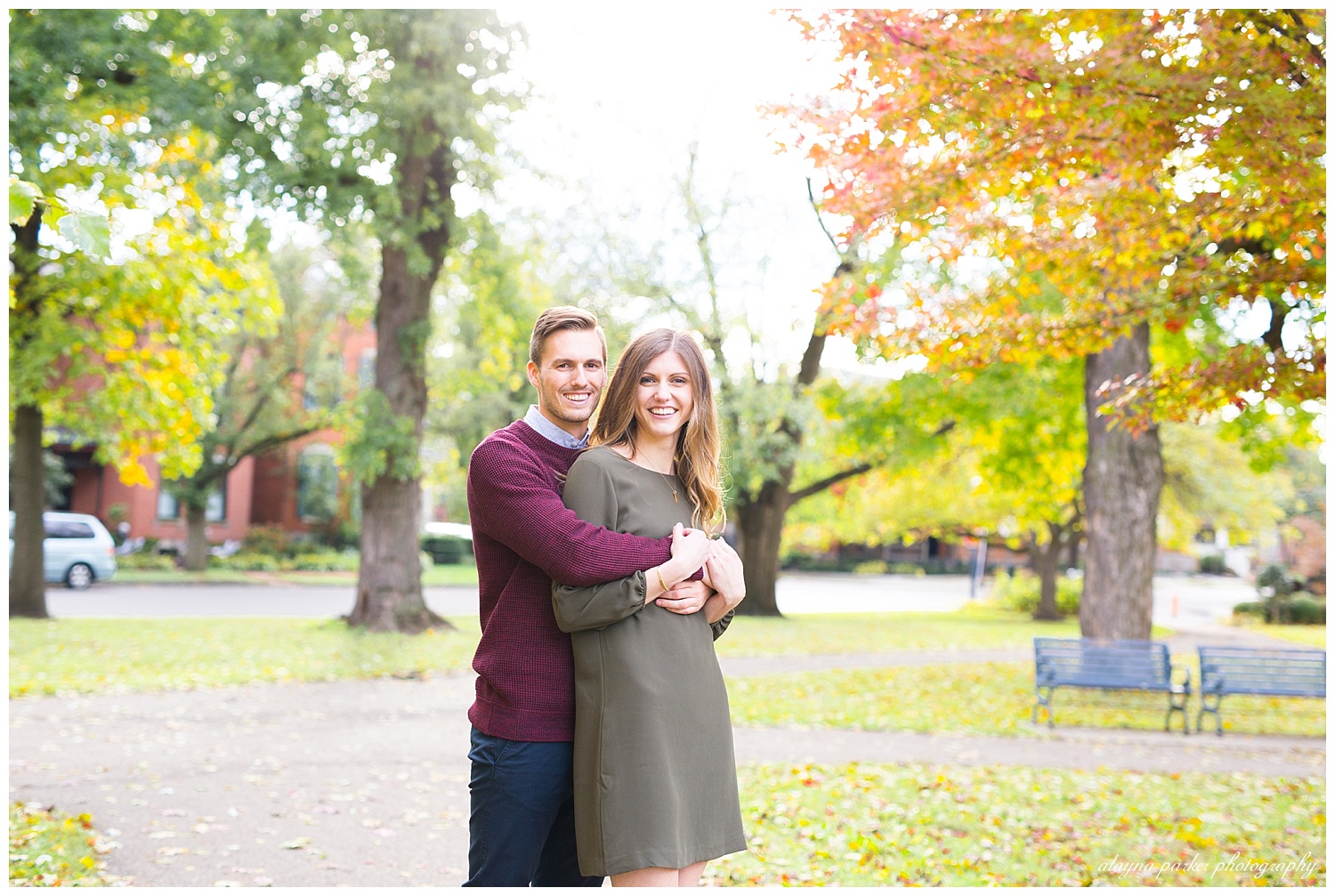 engaged couple smiling at camera with colorful fall trees around schiller park in german village