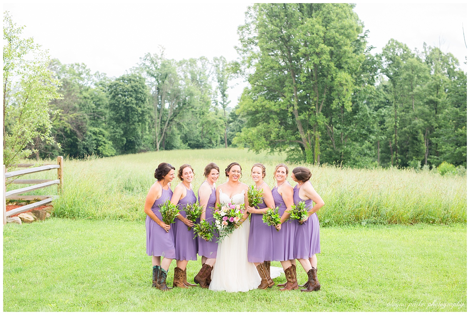 bride and bridesmaids laughing in grassy field at the barn on enchanted acres