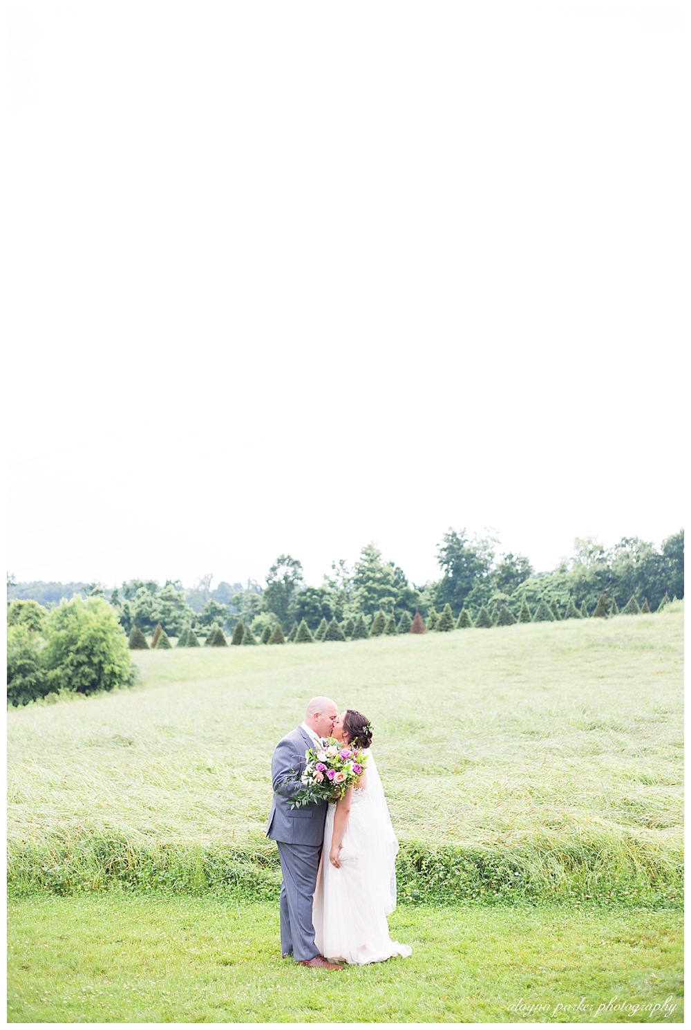 bride and groom kissing in front of grassy field at the barn on enchanted acres
