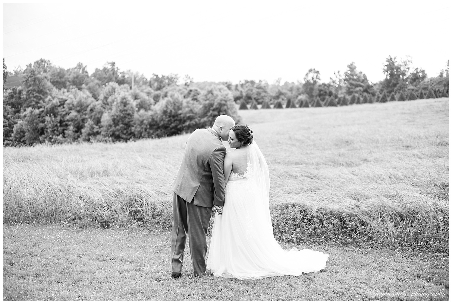 black and white image of groom kissing bride on the cheek at the barn on enchanted acres
