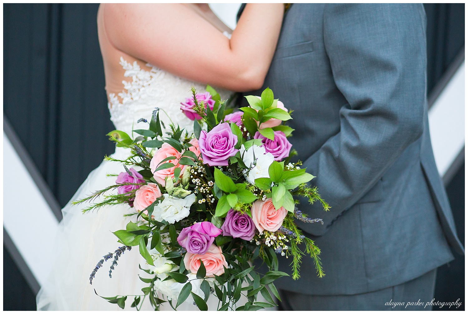 close up of groom holding bride's bouquet while bride embraces groom