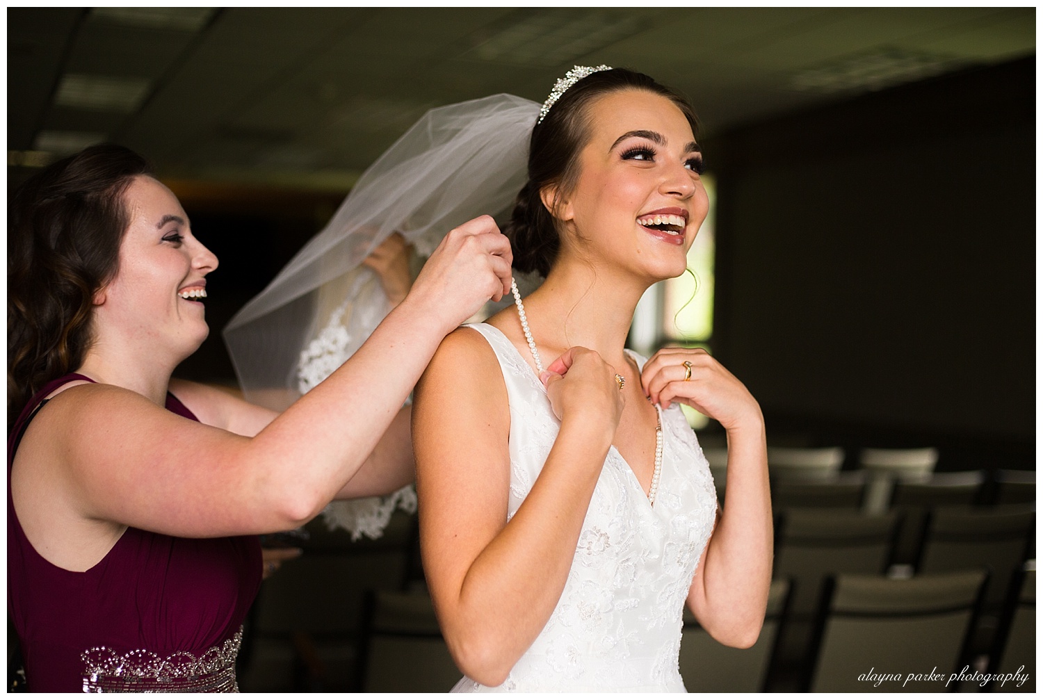 bride laughing as bridesmaid puts necklace on her