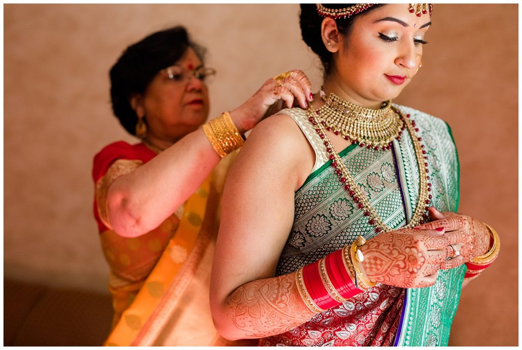 mother of the bride putting on traditional indian jewelry