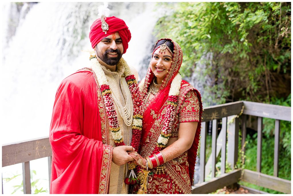 indian bride and groom smiling at camera standing in front of chagrin falls