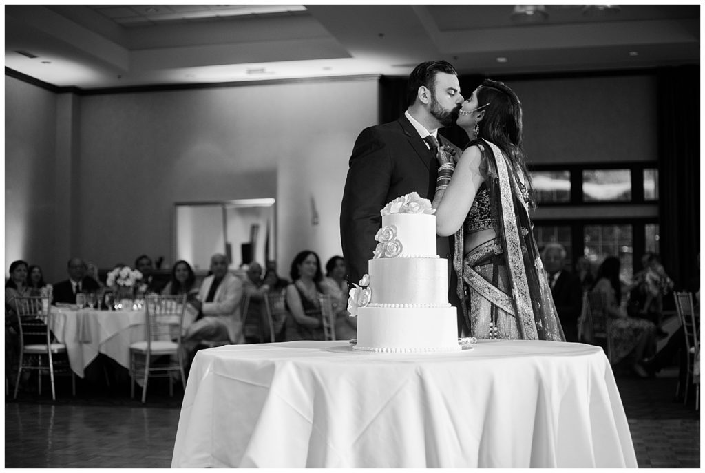 black and white image of bride and groom kissing after cutting cake at bertram inn