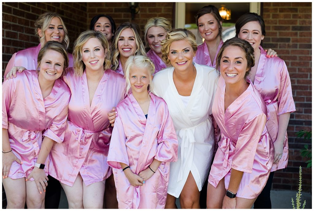 bride in white robe and bridesmaids in pink robes while getting ready
