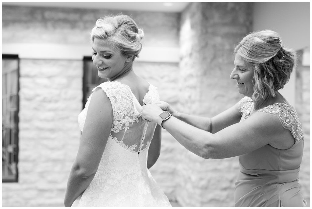 black and white image of mother buttoning bride's wedding dress
