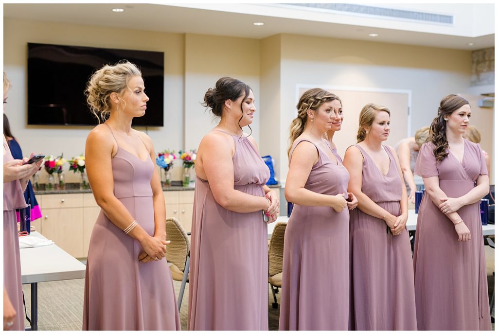 bridesmaids watching bride put on wedding dress