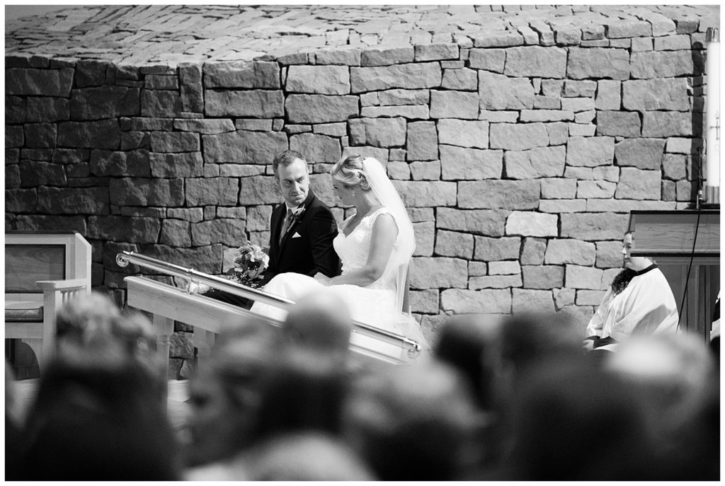 black and white image of bride and groom sitting in church during wedding ceremony