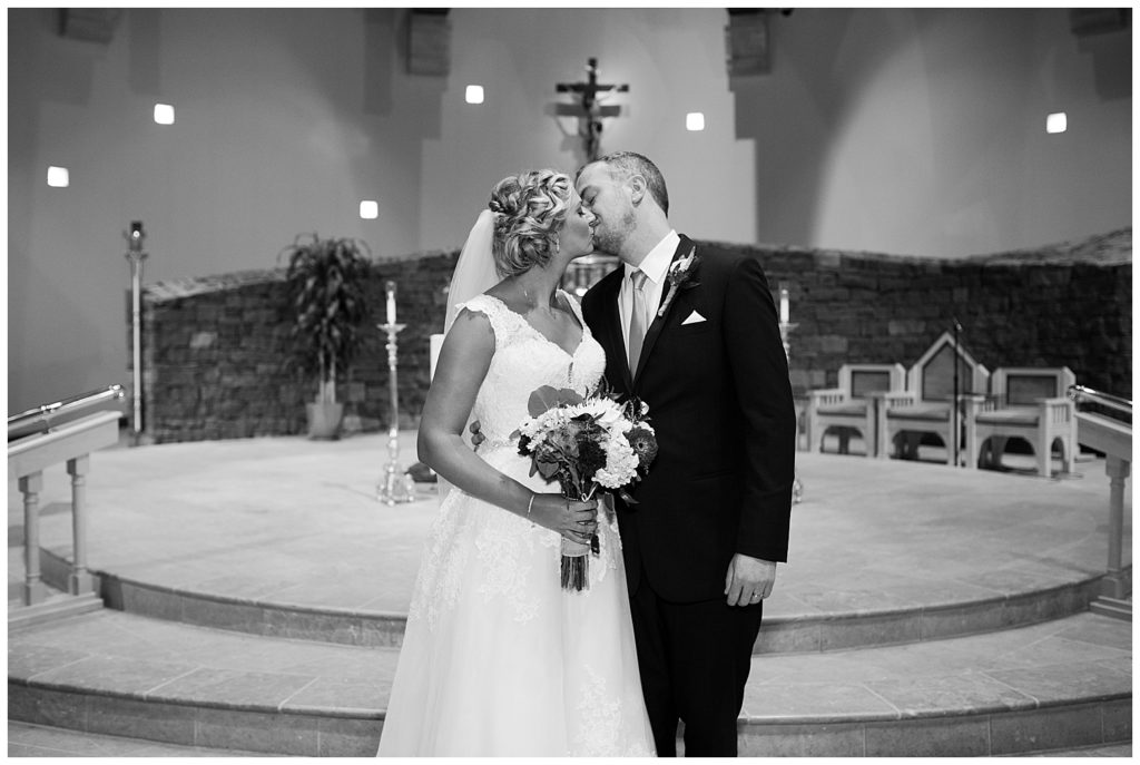 black and white image of bride and groom kissing at alter