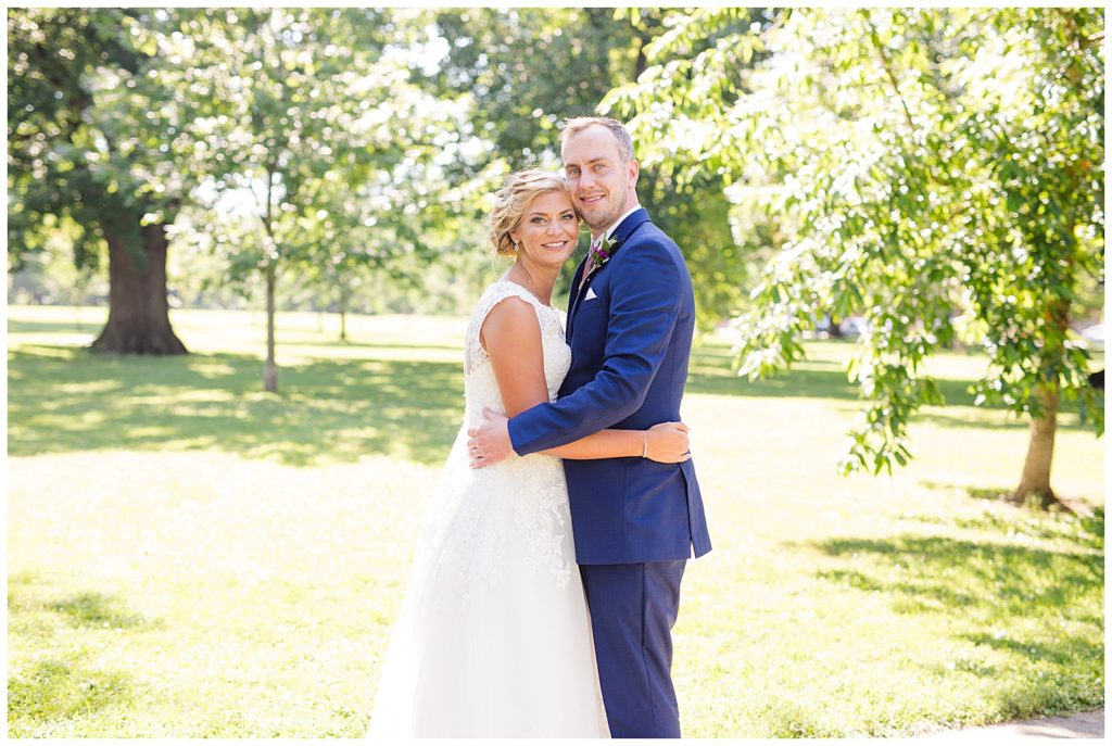 bride and groom holding onto each other and smiling at the camera at schiller park