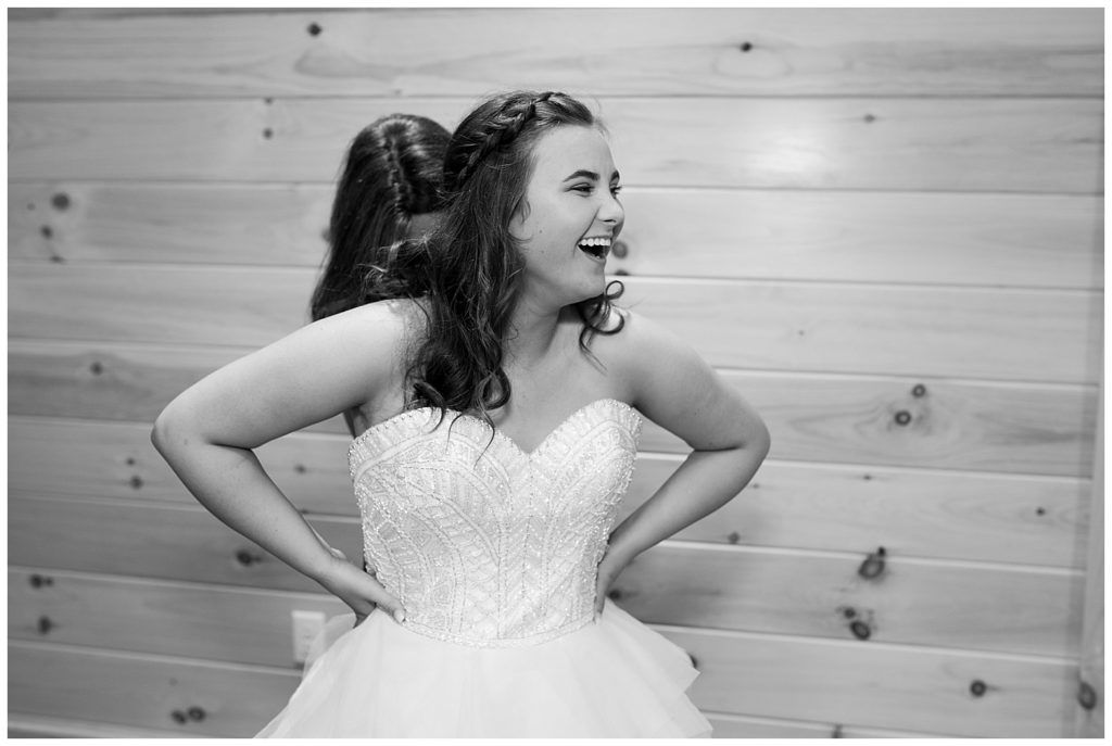 A picture in black and white of the bride laughing as her mother finishes buttoning up her wedding dress at the Cedar Grove Lodge venue in Hocking Hills, Ohio by Columbus wedding photographer, Alayna Parker Photography