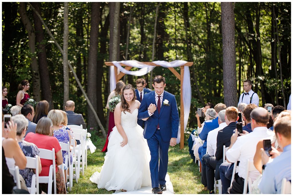 A photograph of the bride and groom smiling and walking down the aisle just after the wedding ceremony as the guests look on at the Cedar Grove Lodge wedding venue by Columbus OH wedding photographer, Alayna Parker Photography