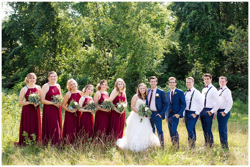 A photograph of the bride and groom with the wedding party lined up and smiling in an outdoor setting at the Cedar Grove Lodge venue in Hocking Hills, Ohio by Columbus OH wedding photographer, Alayna Parker Photography