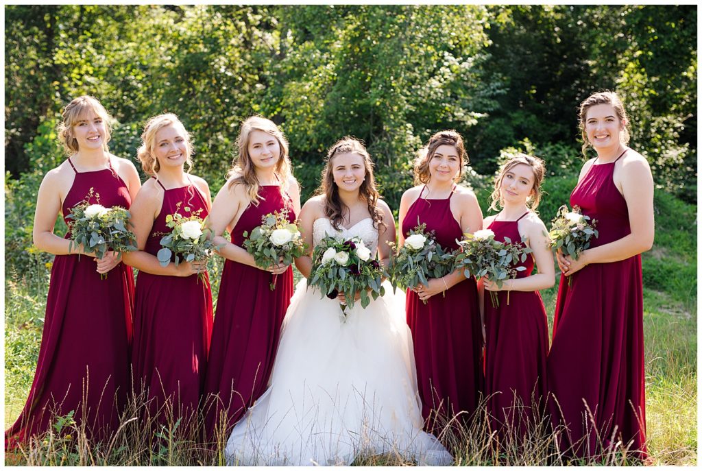 bridesmaids wearing long burgundy dresses and smiling at camera