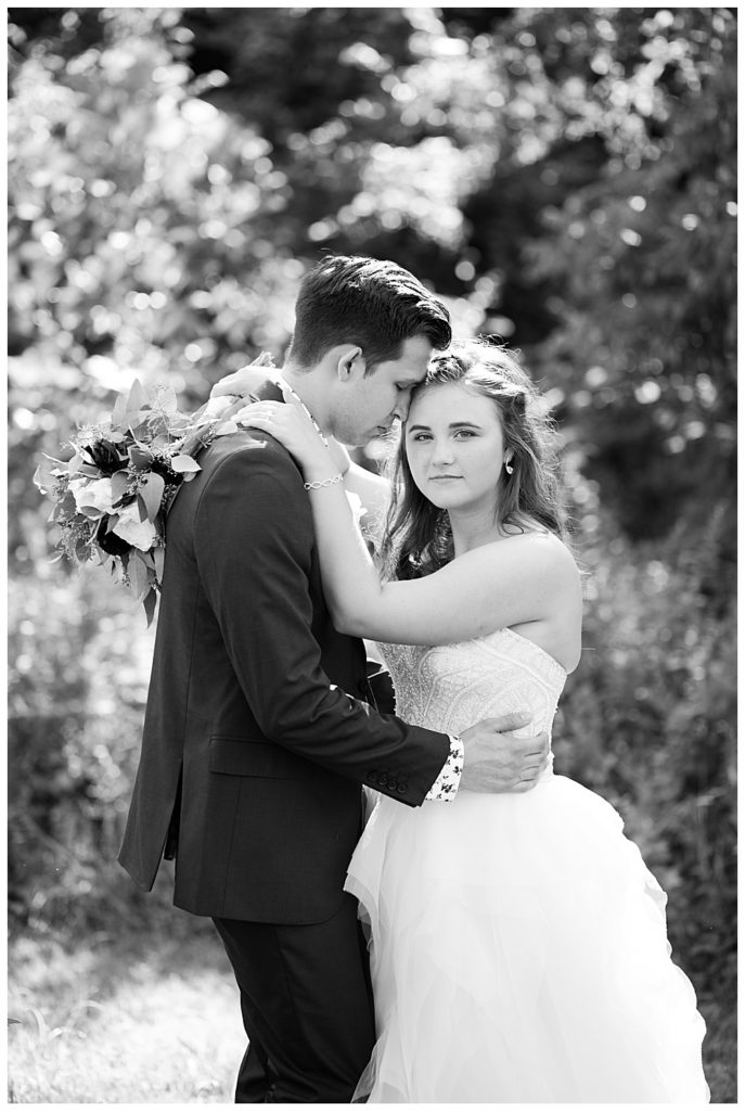 black and white image of bride looking at camera while groom nuzzles into her