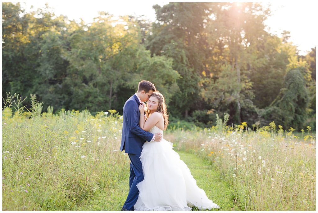 bride closing her eyes and groom holding onto her in field at golden hour at cedar grove lodge