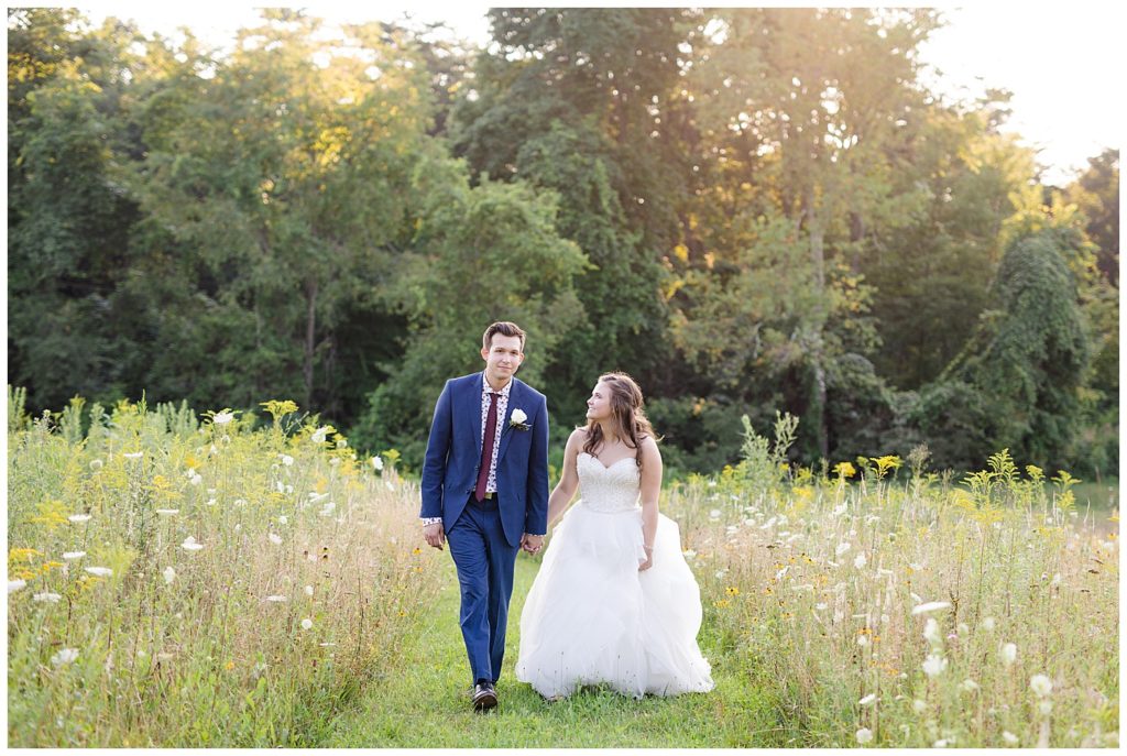 bride and groom walking in field at golden hour at cedar grove lodge
