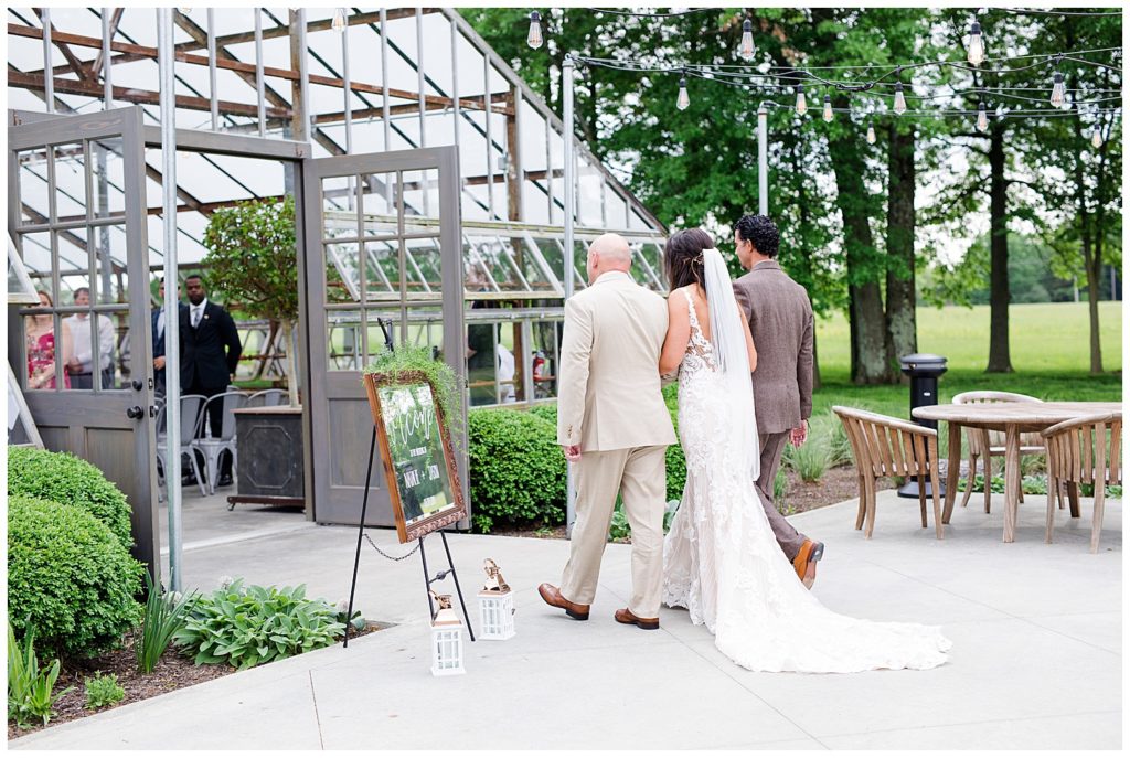 An image of the bride and her father and family member walking the bride into the wedding ceremony hall with her train behind her at the Oak Grove wedding venue by Columbus Ohio wedding photographer, Alayna Parker Photography