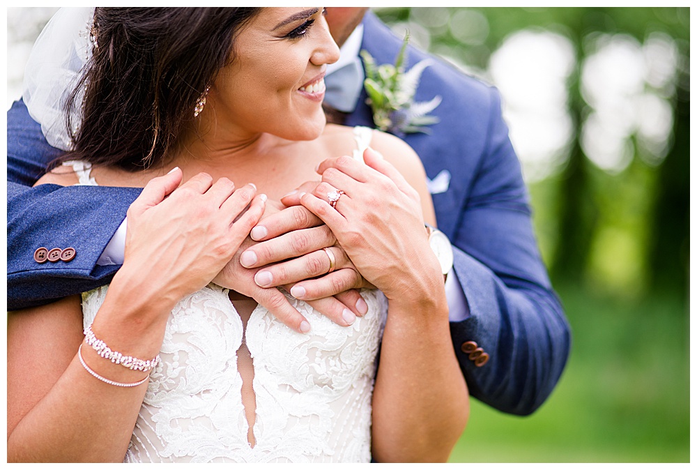 An image of a closeup view of the groom embracing the bride from behind as she smiles and grasps his hands at the Oak Grove wedding venue by Columbus Ohio wedding photographer, Alayna Parker Photography