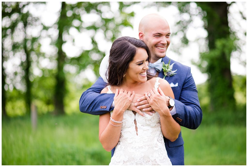 A picture of the groom hugging the bride from behind as they both relax and laugh together at the Oak Grove wedding venue by Columbus wedding photographer, Alayna Parker Photography