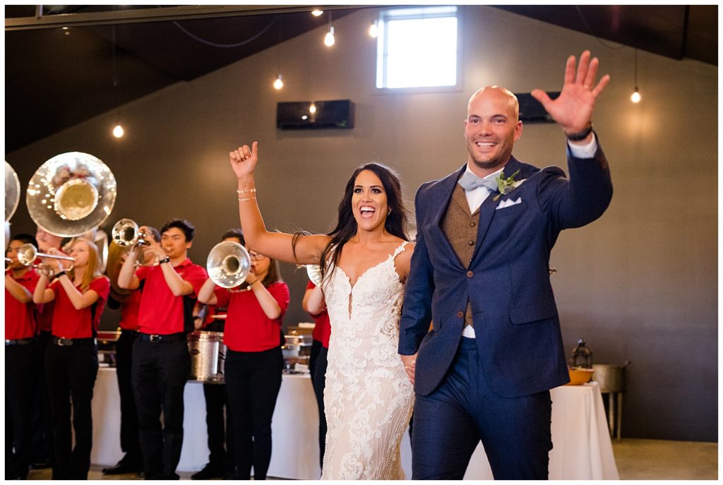 An image of the bride and groom waving and entering the wedding reception party as they're introduced with a band playing at the Oak Grove venue in New Albany, Ohio by Columbus Ohio wedding photographer, Alayna Parker Photography