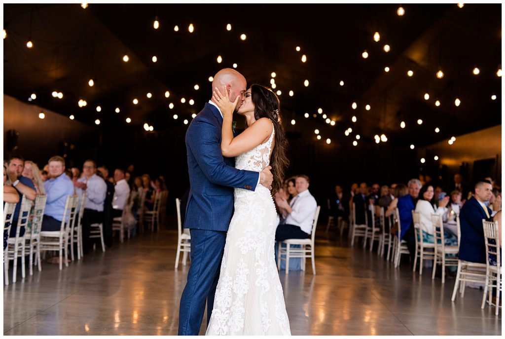 An image of the bride and groom kissing as they end their first dance at the wedding reception while the guests look on and clap at the Oak Grove wedding venue by Columbus Ohio wedding photographer, Alayna Parker Photography
