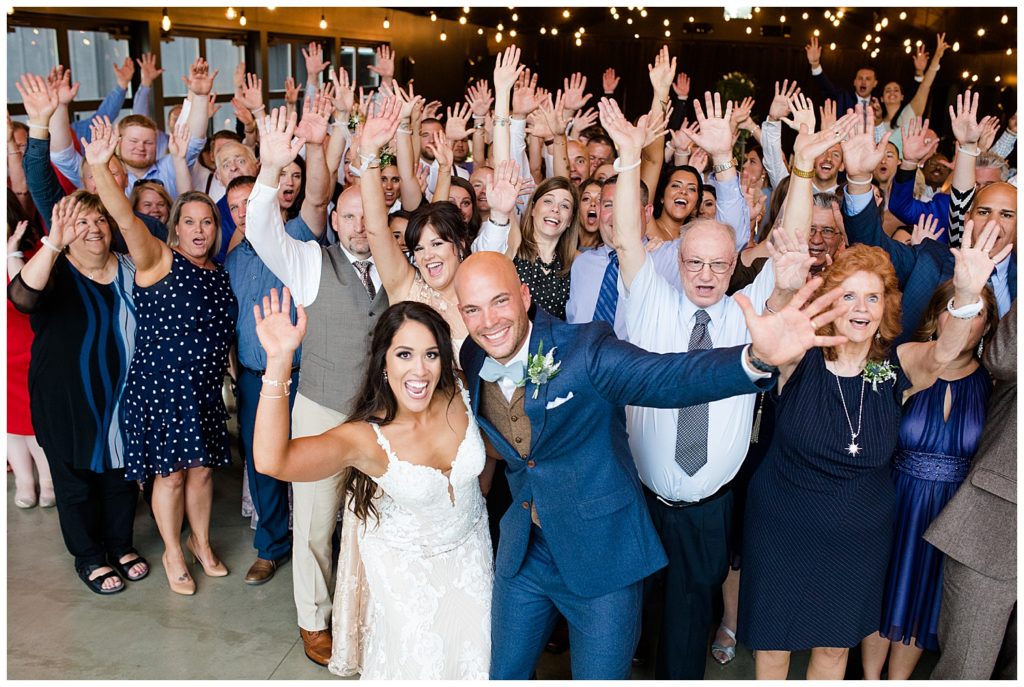 bride and groom take large group photo with guests on the dance floor at jorgensen farms oak grove