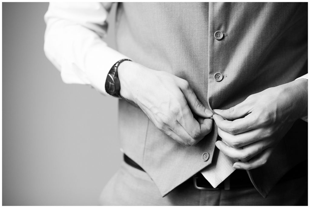 black and white image of groom buttoning vest