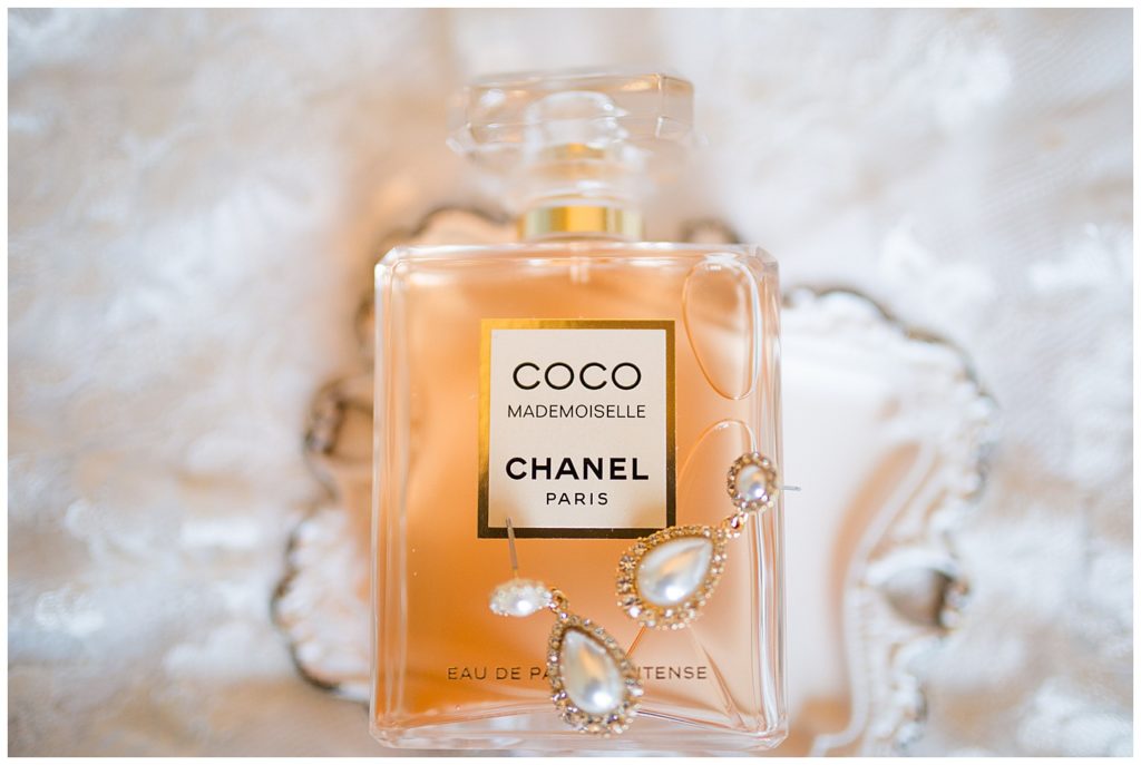 A photograph of a closeup of the bride's earrings and perfume bottle as they lay on a background of her wedding dress by Columbus OH wedding photographer, Alayna Parker Photography