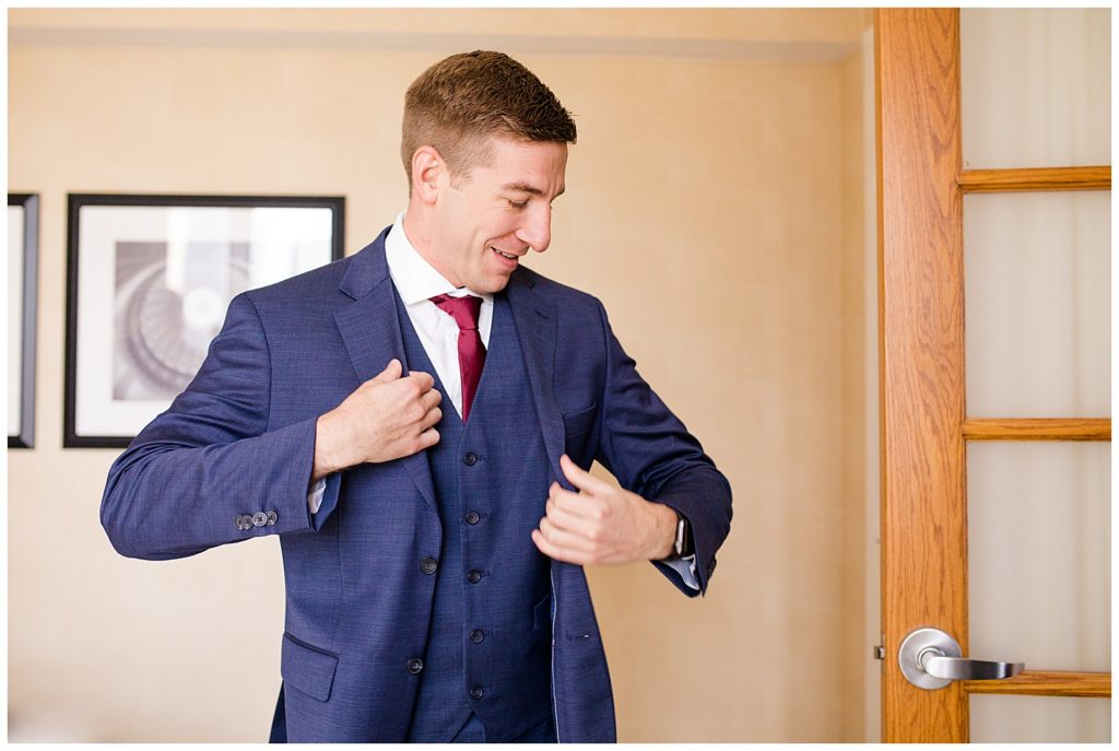 A picture of the groom putting on his tuxedo jacket as he is dressing for the wedding ceremony by Columbus wedding photographer, Alayna Parker Photography