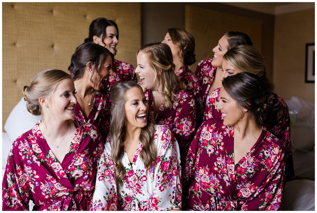 A photograph of a bride and her bridesmaids smiling and relaxing together in their matching robes before the wedding ceremony by Columbus OH wedding photographer, Alayna Parker Photography